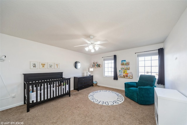 carpeted bedroom with a crib, a ceiling fan, and baseboards