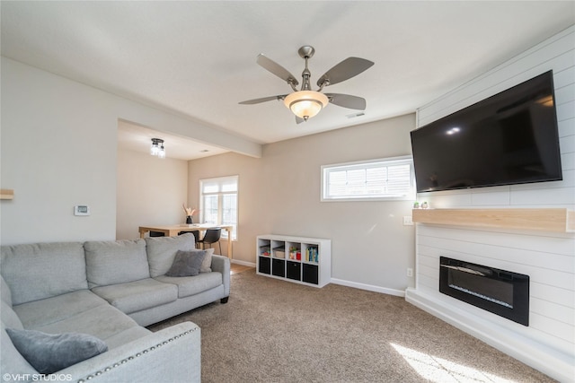 carpeted living area featuring visible vents, baseboards, a ceiling fan, and a glass covered fireplace