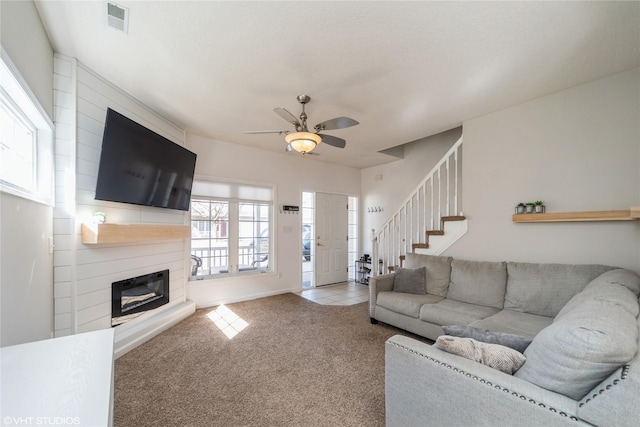 living room featuring visible vents, a large fireplace, carpet, ceiling fan, and stairs