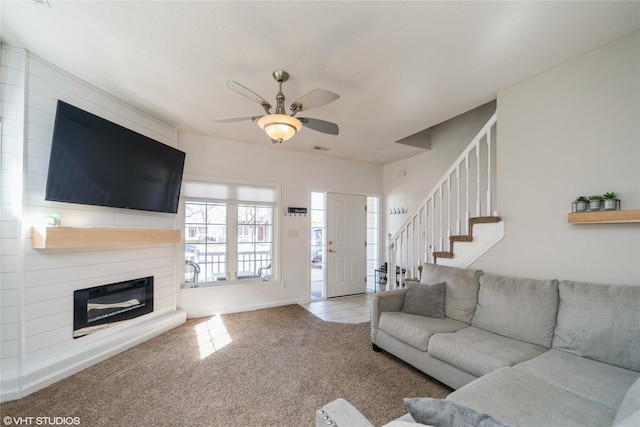 living room featuring a ceiling fan, stairs, a glass covered fireplace, tile patterned floors, and carpet flooring