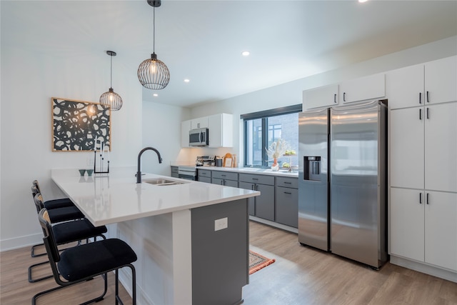 kitchen featuring a sink, a kitchen breakfast bar, light wood-style floors, appliances with stainless steel finishes, and a peninsula