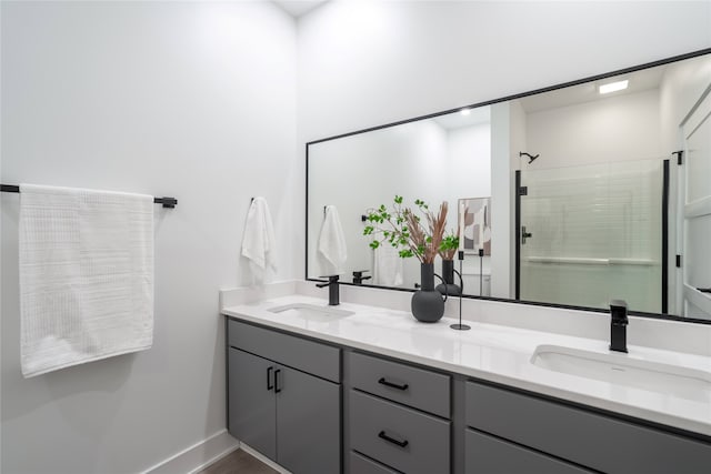 bathroom featuring double vanity, tiled shower, baseboards, and a sink