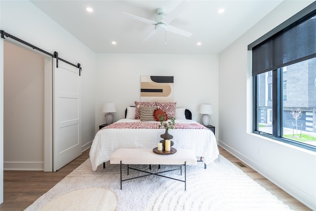 bedroom with recessed lighting, baseboards, a barn door, and wood finished floors