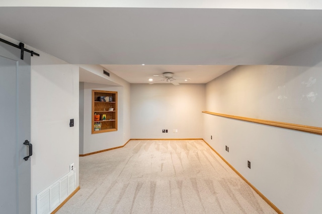 empty room with visible vents, built in features, a barn door, baseboards, and ceiling fan