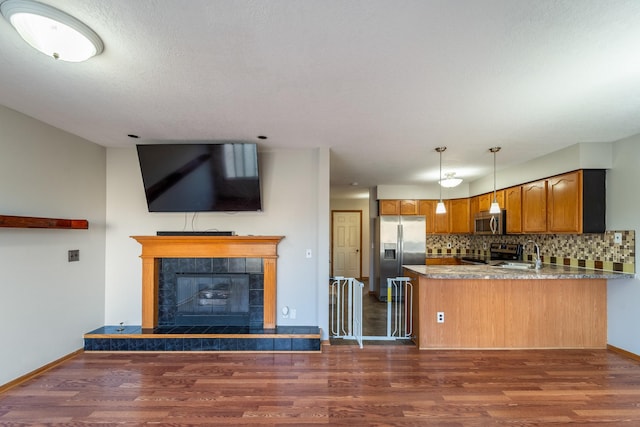 kitchen with backsplash, dark wood finished floors, appliances with stainless steel finishes, a peninsula, and brown cabinetry