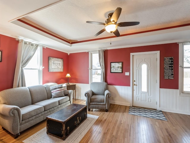 living room with hardwood / wood-style floors, a tray ceiling, ceiling fan, and wainscoting