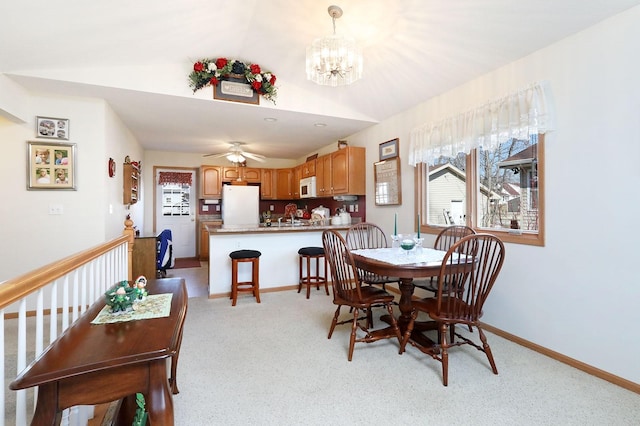 dining room featuring lofted ceiling, ceiling fan with notable chandelier, baseboards, and light carpet