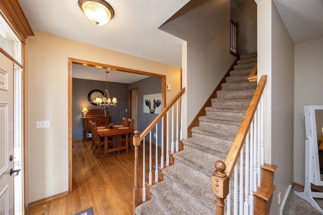 staircase featuring a textured ceiling, wood finished floors, baseboards, and a chandelier