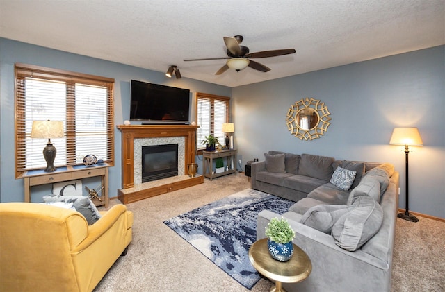 carpeted living area featuring baseboards, a glass covered fireplace, a textured ceiling, and ceiling fan