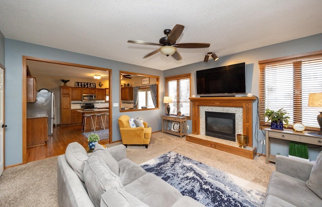 living room with a glass covered fireplace, a ceiling fan, baseboards, and dark colored carpet