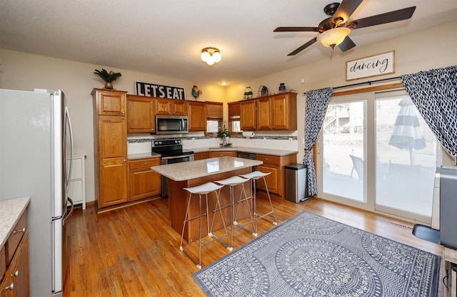 kitchen featuring a breakfast bar area, wood finished floors, brown cabinetry, a kitchen island, and appliances with stainless steel finishes