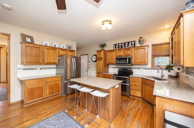 kitchen with a sink, a kitchen breakfast bar, appliances with stainless steel finishes, and light wood finished floors