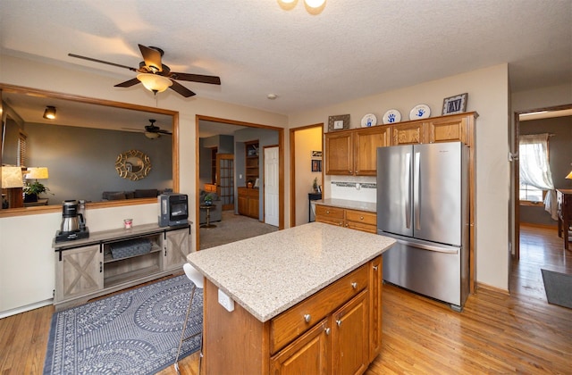 kitchen with brown cabinets, light wood-type flooring, freestanding refrigerator, and ceiling fan