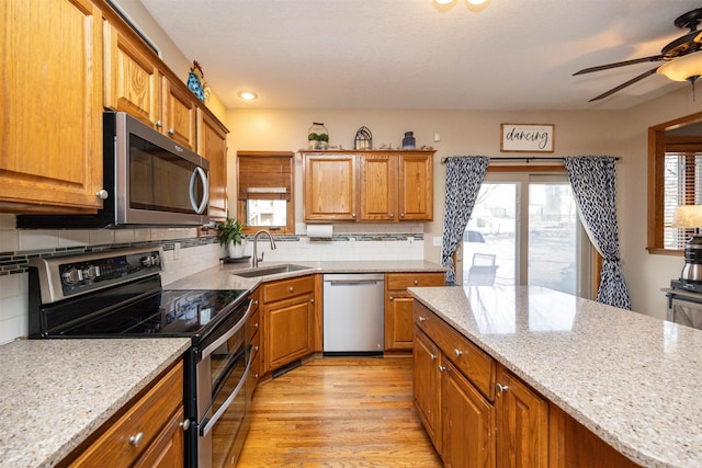 kitchen featuring brown cabinetry, a sink, ceiling fan, stainless steel appliances, and light wood-style floors