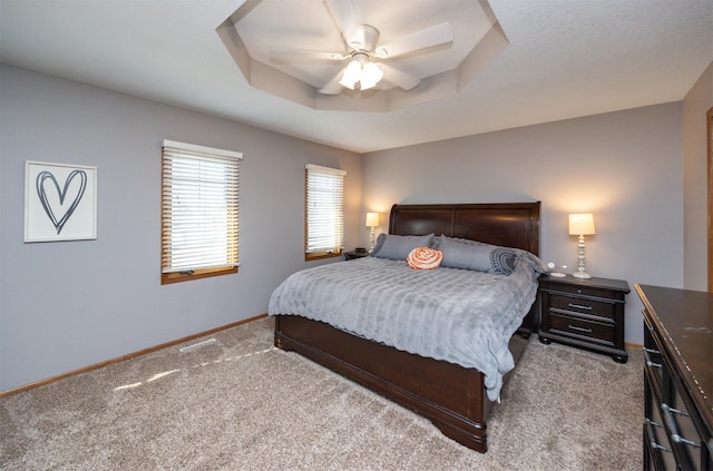 carpeted bedroom featuring a tray ceiling, baseboards, visible vents, and ceiling fan