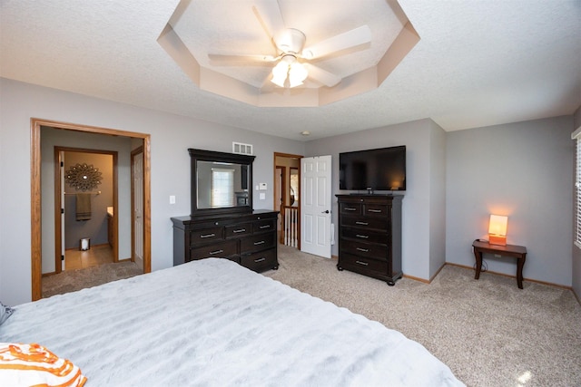 bedroom featuring a ceiling fan, visible vents, baseboards, a tray ceiling, and light carpet