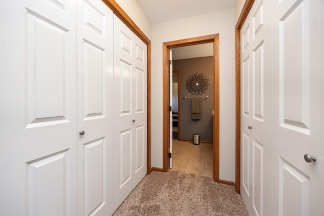 corridor featuring light tile patterned floors, baseboards, and light carpet