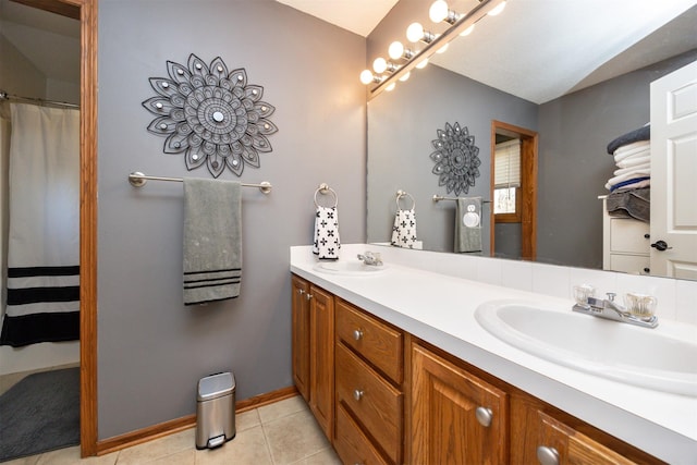 full bathroom featuring tile patterned flooring, double vanity, baseboards, and a sink