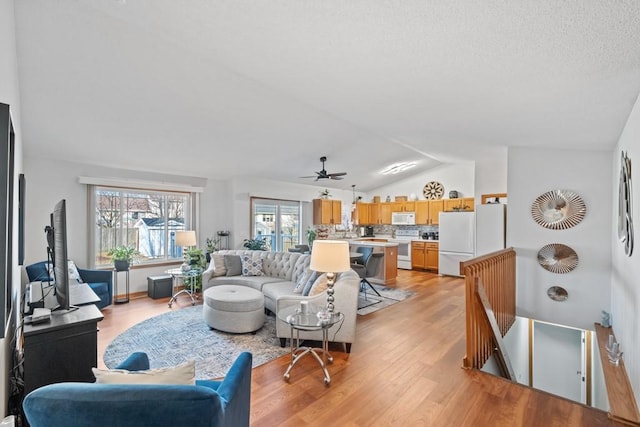 living room featuring ceiling fan, light wood-style floors, and vaulted ceiling