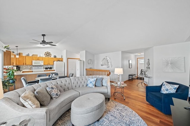 living area with light wood-style floors, a ceiling fan, and vaulted ceiling