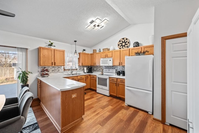 kitchen featuring a sink, white appliances, light wood-style floors, a peninsula, and light countertops