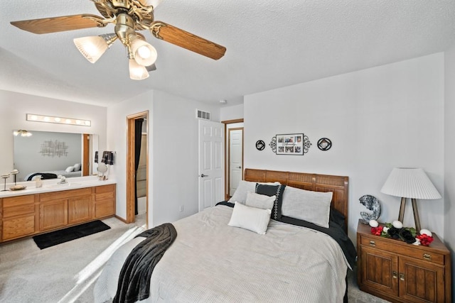 bedroom featuring a ceiling fan, visible vents, a textured ceiling, light colored carpet, and connected bathroom