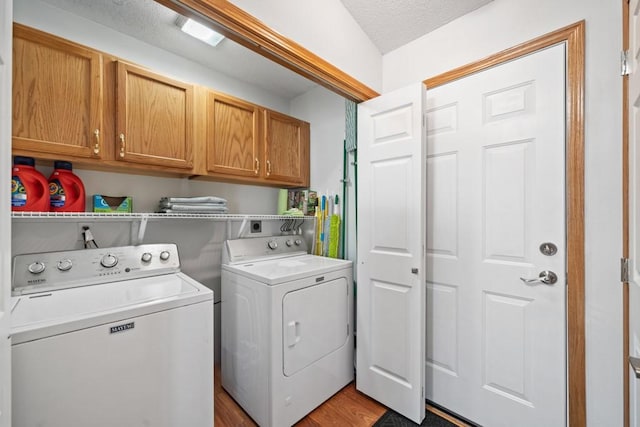 laundry area with cabinet space, independent washer and dryer, light wood finished floors, and a textured ceiling