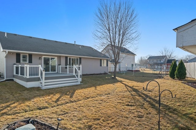 back of property featuring a wooden deck, a lawn, a shingled roof, and fence