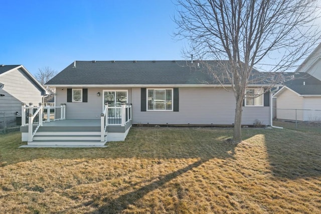 rear view of property with a deck, a yard, fence, and a shingled roof