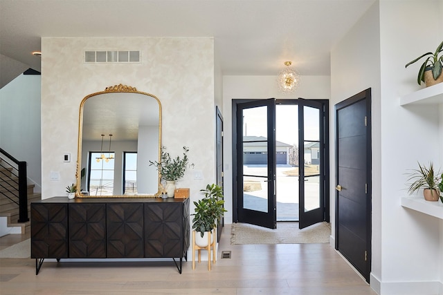 foyer featuring visible vents, wood finished floors, french doors, an inviting chandelier, and stairs