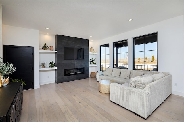 living area featuring recessed lighting, a fireplace, baseboards, and light wood-style floors