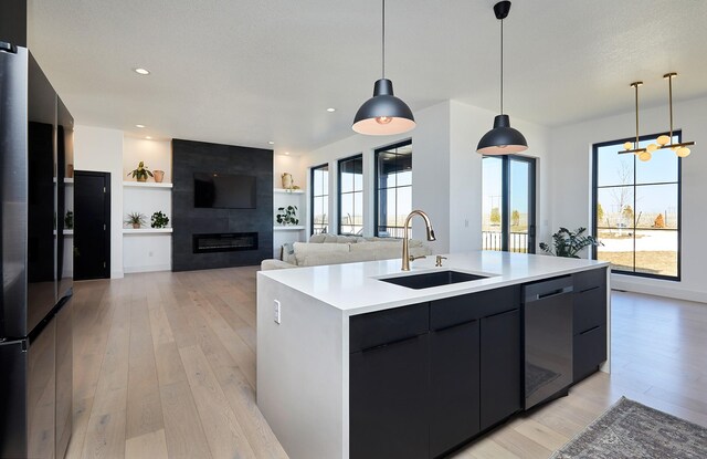 kitchen with a sink, a center island with sink, light wood-type flooring, modern cabinets, and stainless steel dishwasher