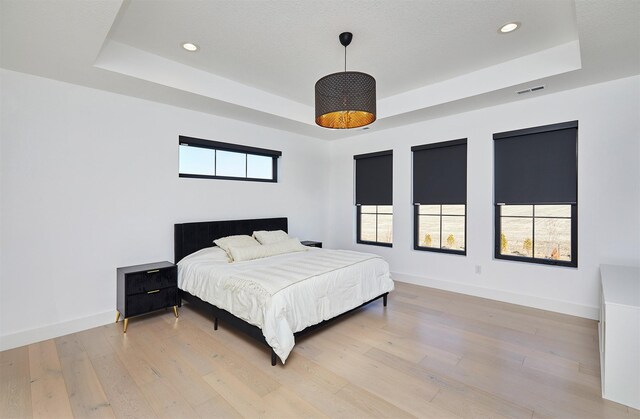 bedroom featuring a raised ceiling, visible vents, baseboards, and light wood finished floors