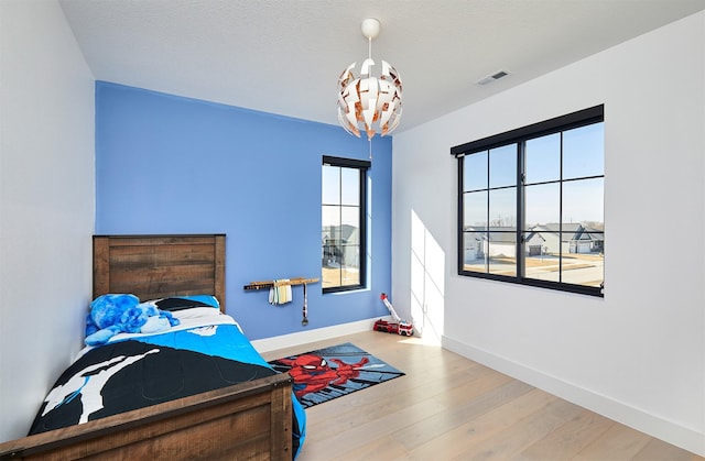 bedroom with visible vents, baseboards, wood finished floors, and a chandelier