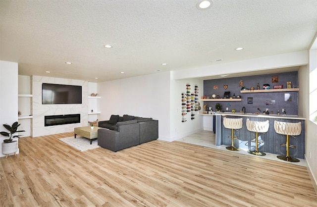 living area with recessed lighting, a fireplace, indoor wet bar, a textured ceiling, and light wood-type flooring