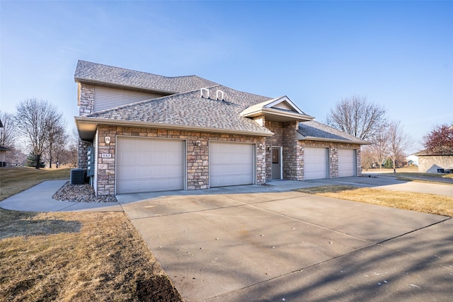 view of front of house featuring cooling unit, roof with shingles, an attached garage, concrete driveway, and stone siding