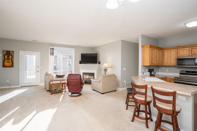 kitchen featuring a sink, light countertops, appliances with stainless steel finishes, light colored carpet, and open floor plan