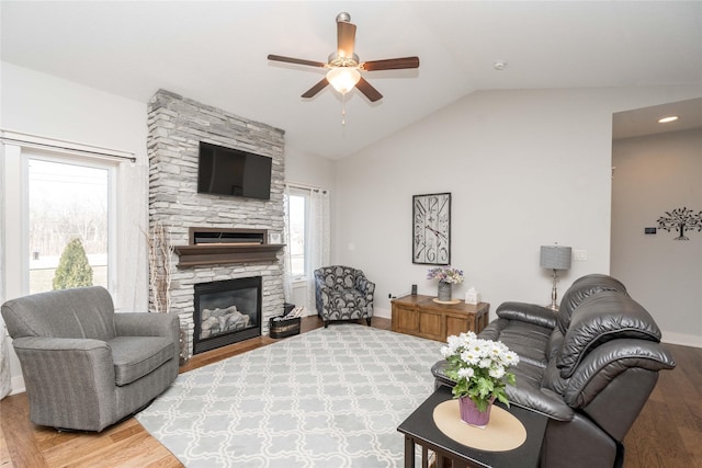 living area featuring lofted ceiling, light wood-style floors, a stone fireplace, and a ceiling fan