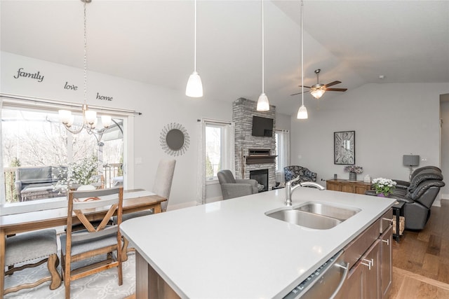 kitchen featuring light wood finished floors, open floor plan, ceiling fan with notable chandelier, a fireplace, and a sink