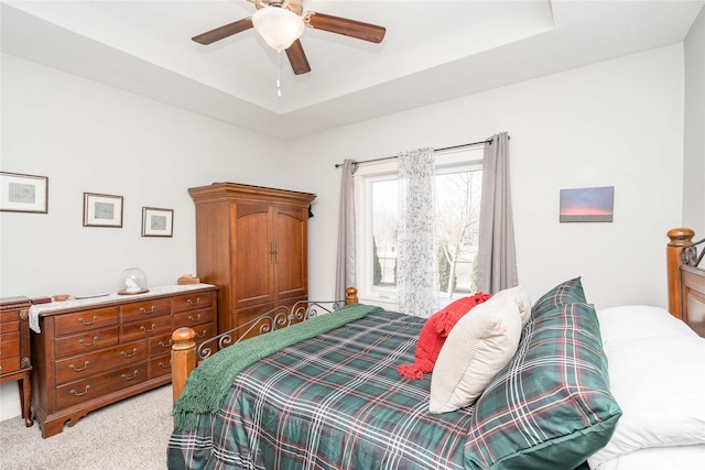 bedroom featuring light colored carpet, a ceiling fan, and a tray ceiling