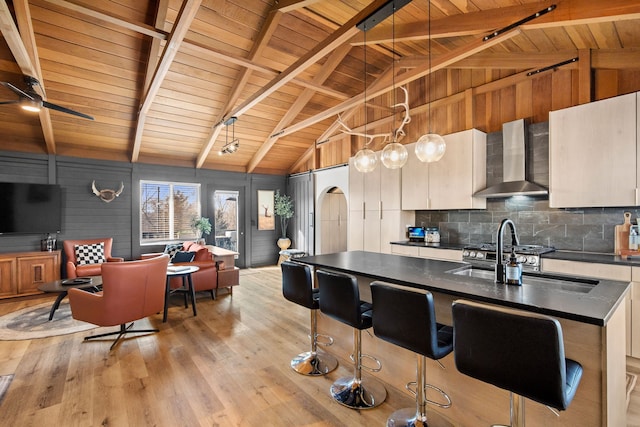 kitchen with dark countertops, wall chimney range hood, light wood-type flooring, decorative backsplash, and wooden ceiling