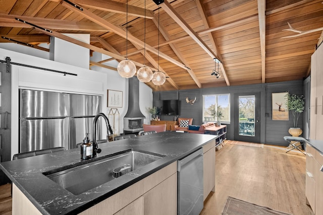 kitchen with open floor plan, a wood stove, light wood-style floors, stainless steel appliances, and a sink