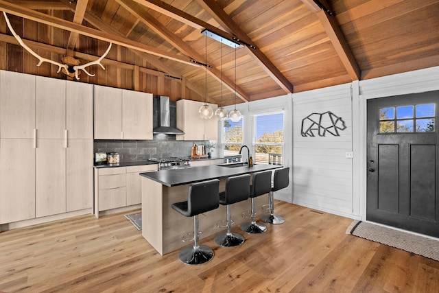 kitchen with dark countertops, wall chimney range hood, wood ceiling, light wood-type flooring, and a sink