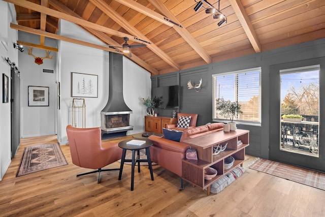 living area featuring wood finished floors, visible vents, a wood stove, vaulted ceiling with beams, and wooden ceiling