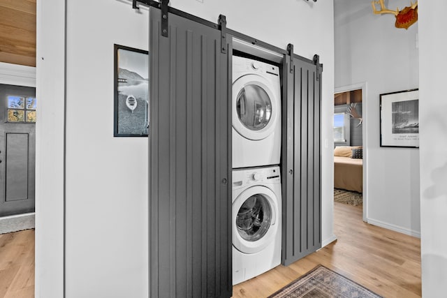 washroom with stacked washing maching and dryer, a barn door, light wood finished floors, baseboards, and laundry area