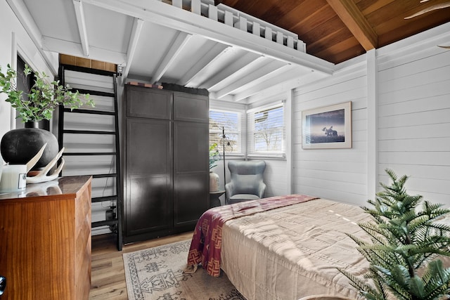 bedroom with beamed ceiling, wooden walls, and light wood-style flooring