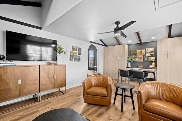 sitting room featuring vaulted ceiling with beams, baseboards, light wood-type flooring, arched walkways, and a ceiling fan