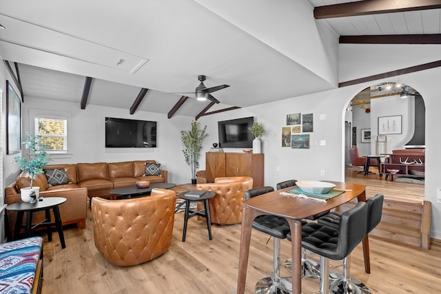 living area featuring arched walkways, vaulted ceiling with beams, light wood-type flooring, and a ceiling fan