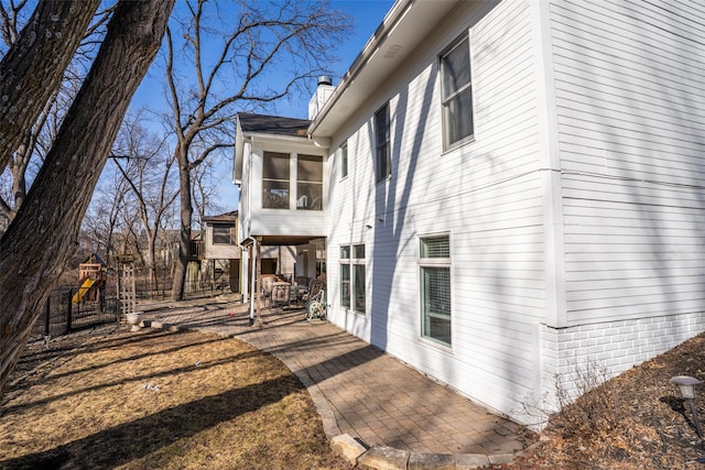 view of side of home featuring a sunroom, a playground, a chimney, and a patio area