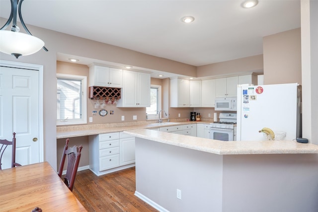 kitchen with light countertops, a peninsula, white cabinets, white appliances, and a sink